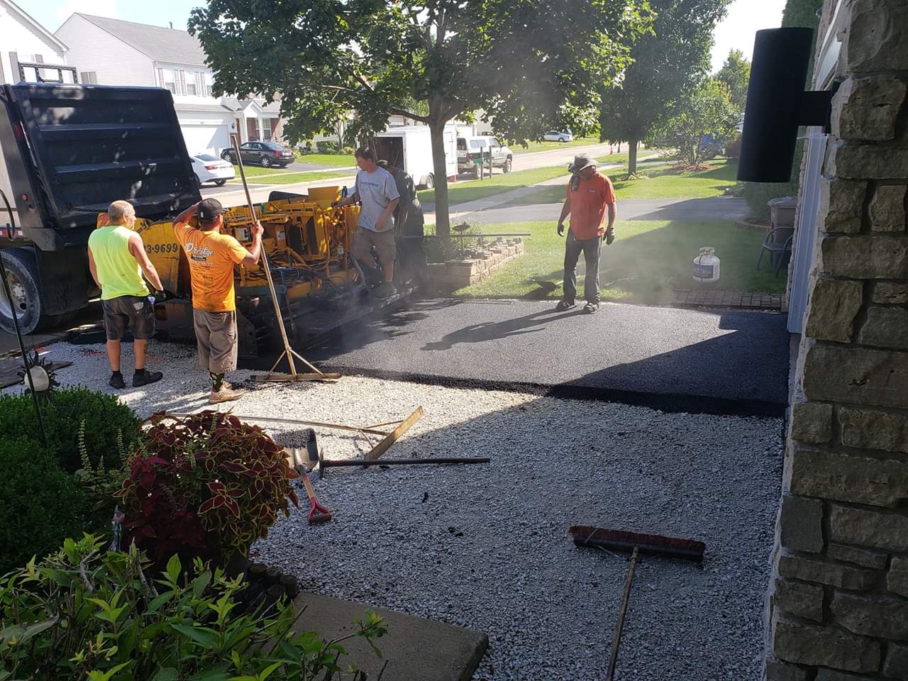 Asphalt paving crew laying blacktop driveway in front of a house.