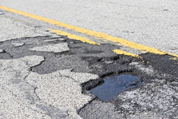 Damaged asphalt road surface with potholes and yellow lane lines.