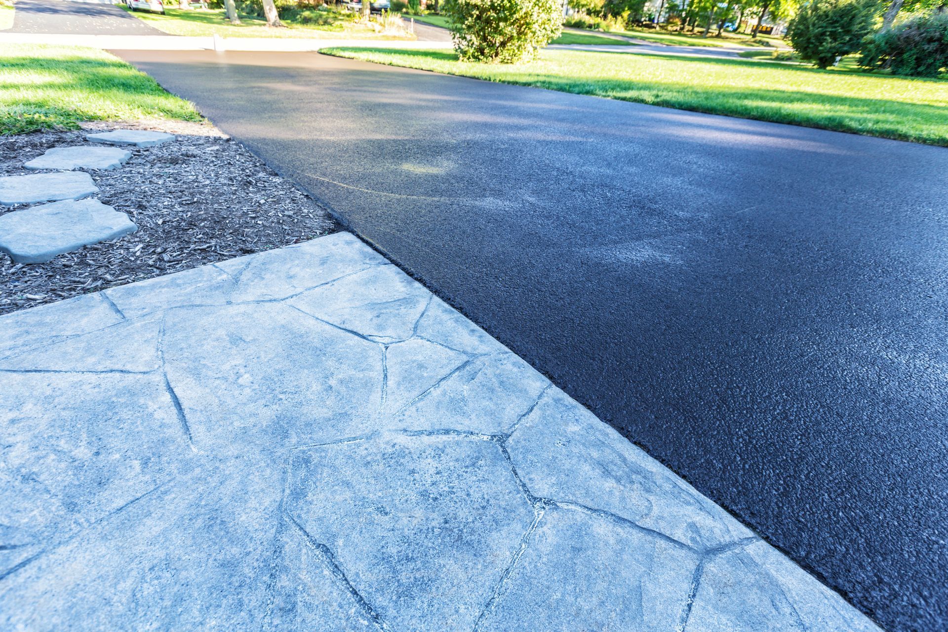Black asphalt driveway and gray patterned concrete border with green grass.