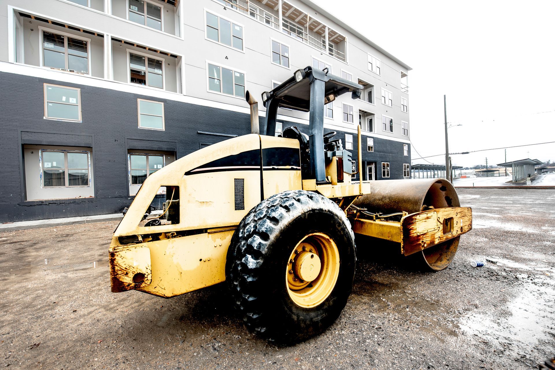 Yellow steamroller in front of a multi-story building under construction.