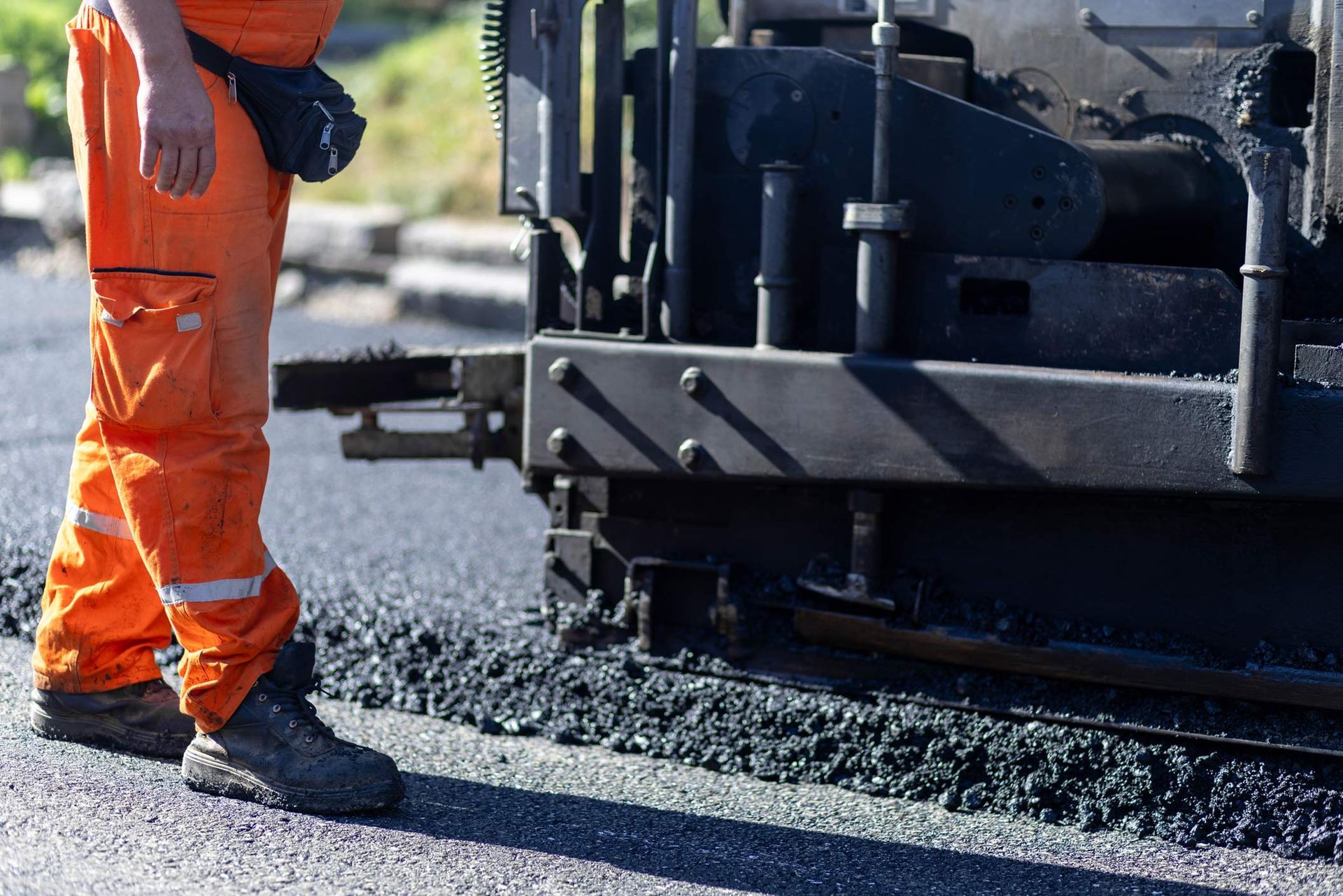 Paving contractor in an orange uniform standing beside an asphalt paver laying fresh asphalt. Paving contractor in an orange uniform standing beside an asphalt paver laying fresh asphalt.