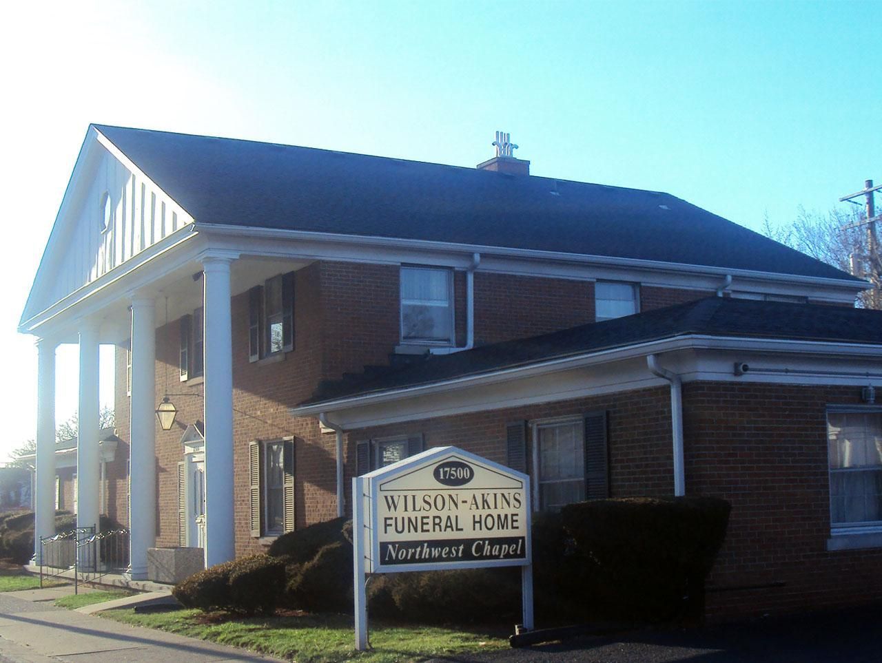 Wilson-Akins Funeral Home with white columns and sign. Brick building with dark roof.