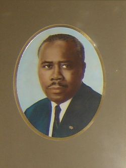 Oval portrait of a man in a dark suit and tie, against a light blue background.