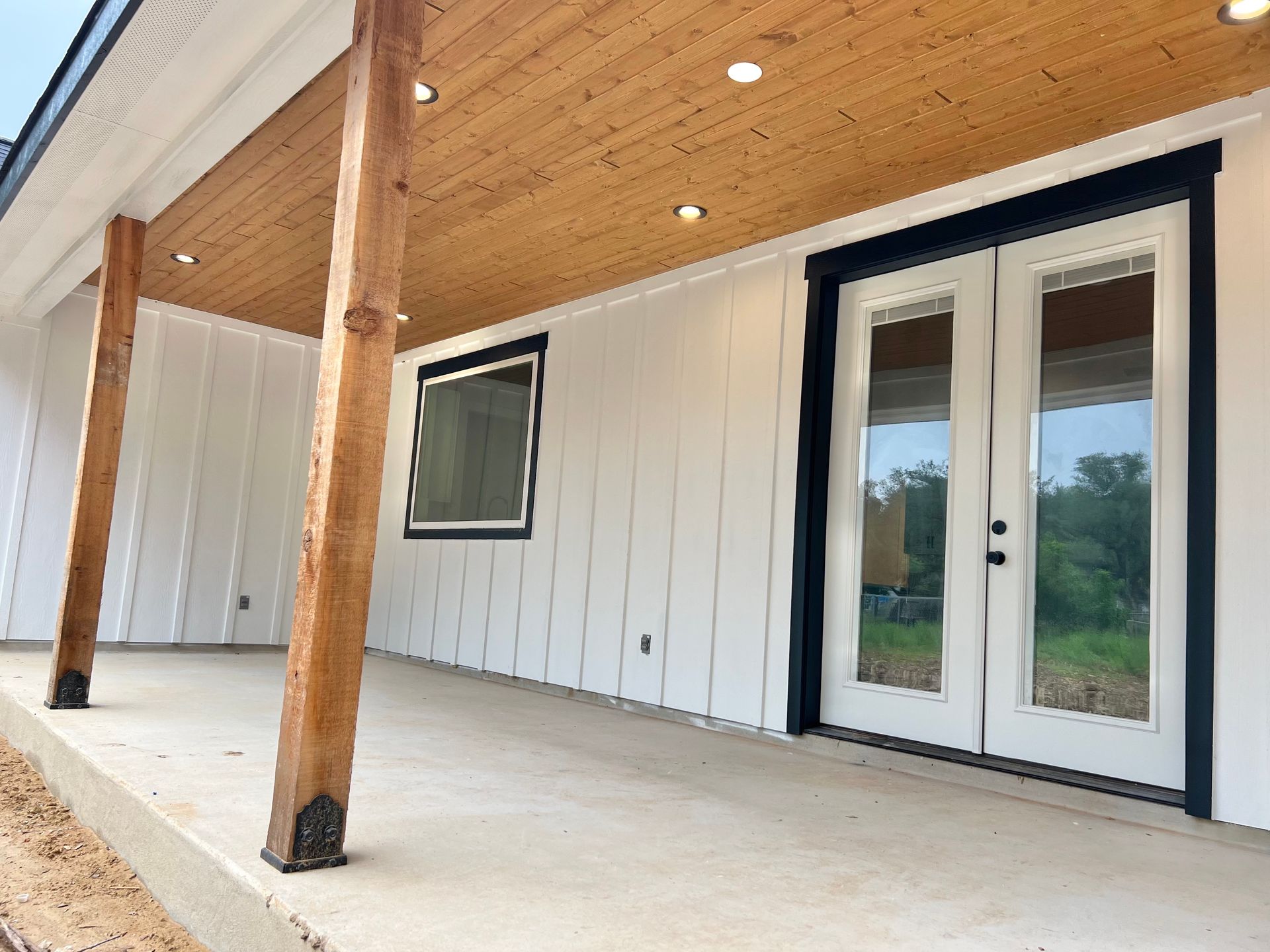 Covered porch with white siding, wood ceiling, and double glass doors on a modern house