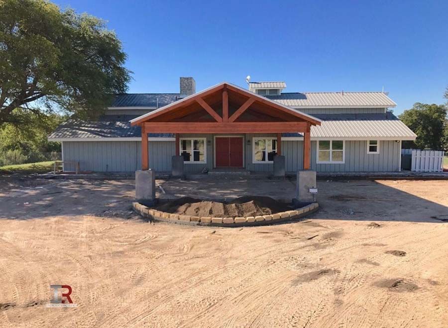 Single-story house with a covered front porch and a circular dirt driveway under a clear blue sky