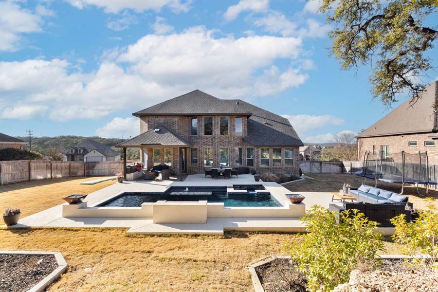 Modern stone house with a large backyard pool and patio under a bright blue sky