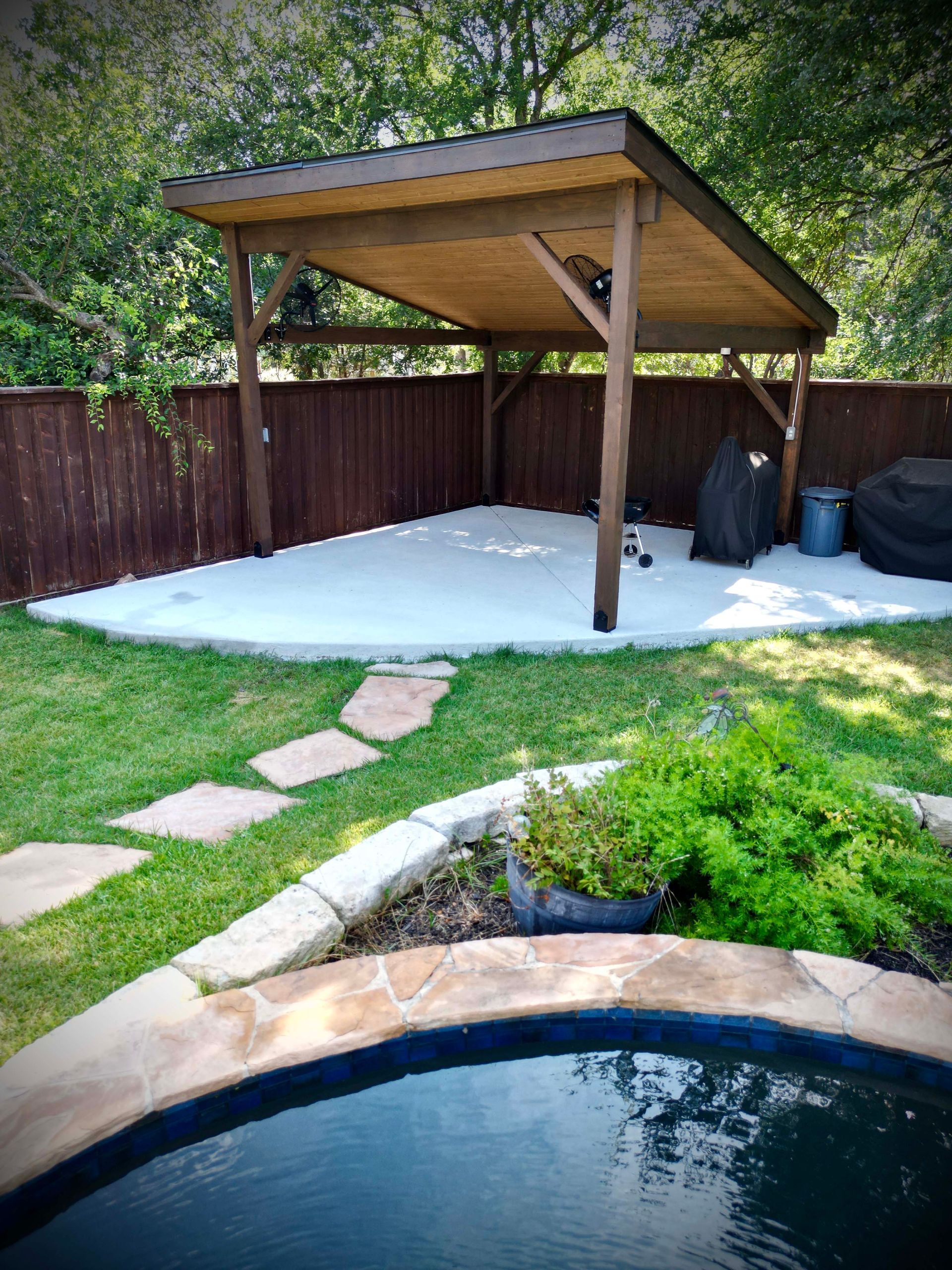 Backyard patio with wooden gazebo, stone path, and pool edge beside a fenced lawn