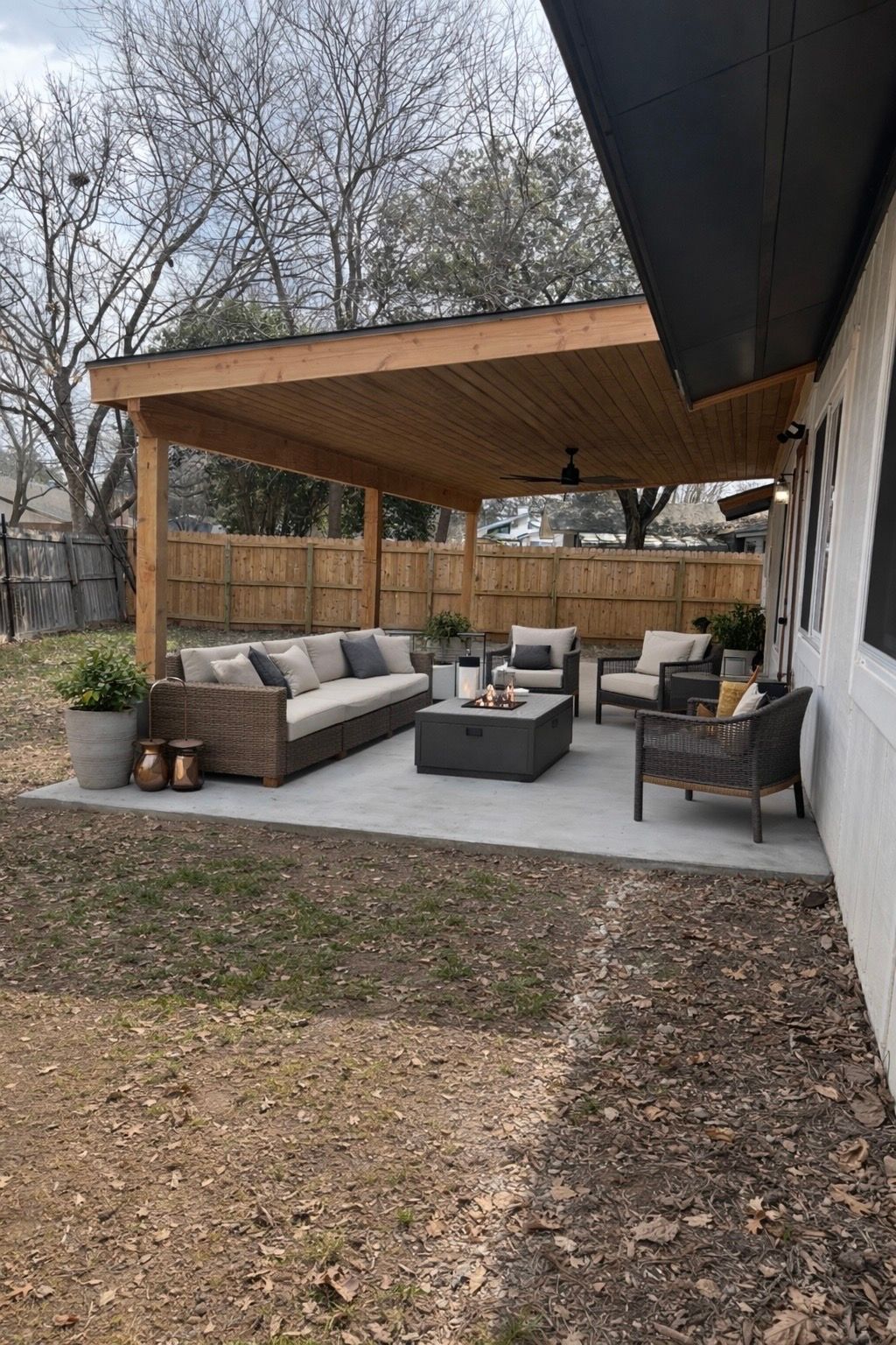 Covered backyard patio with gray sofas, a coffee table, and wooden pergola seating area.