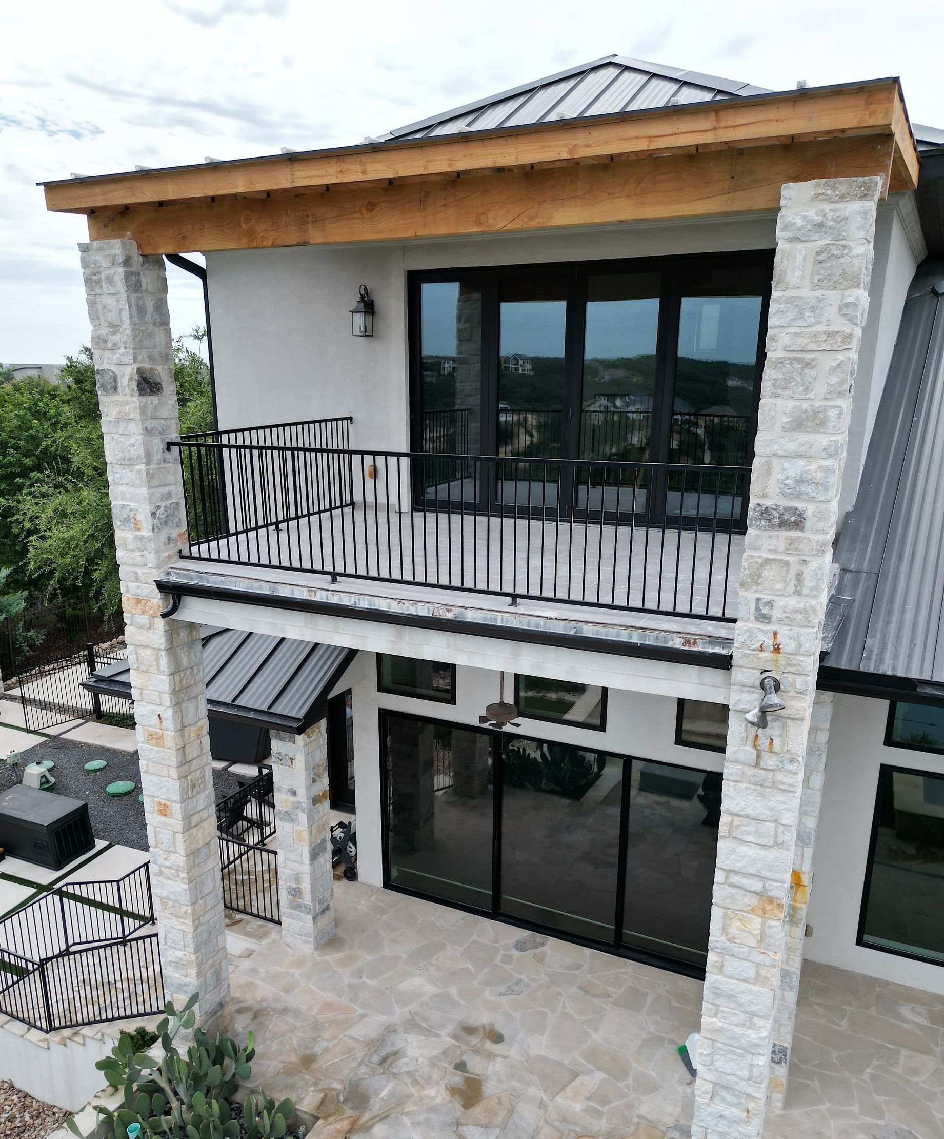 Modern two-story house with stone columns, black balcony railing, and large glass doors