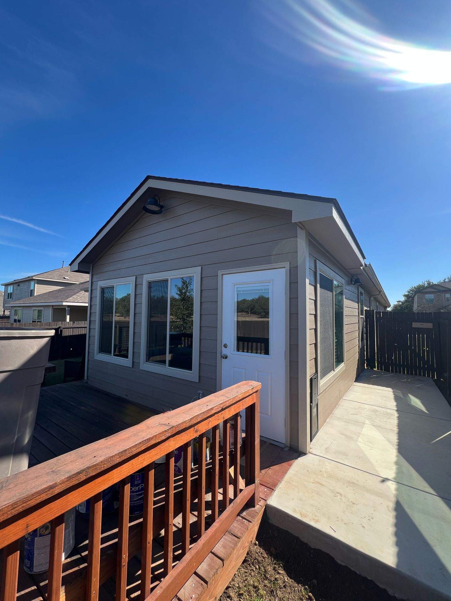 Small beige house with large windows and a wooden deck under a bright blue sky