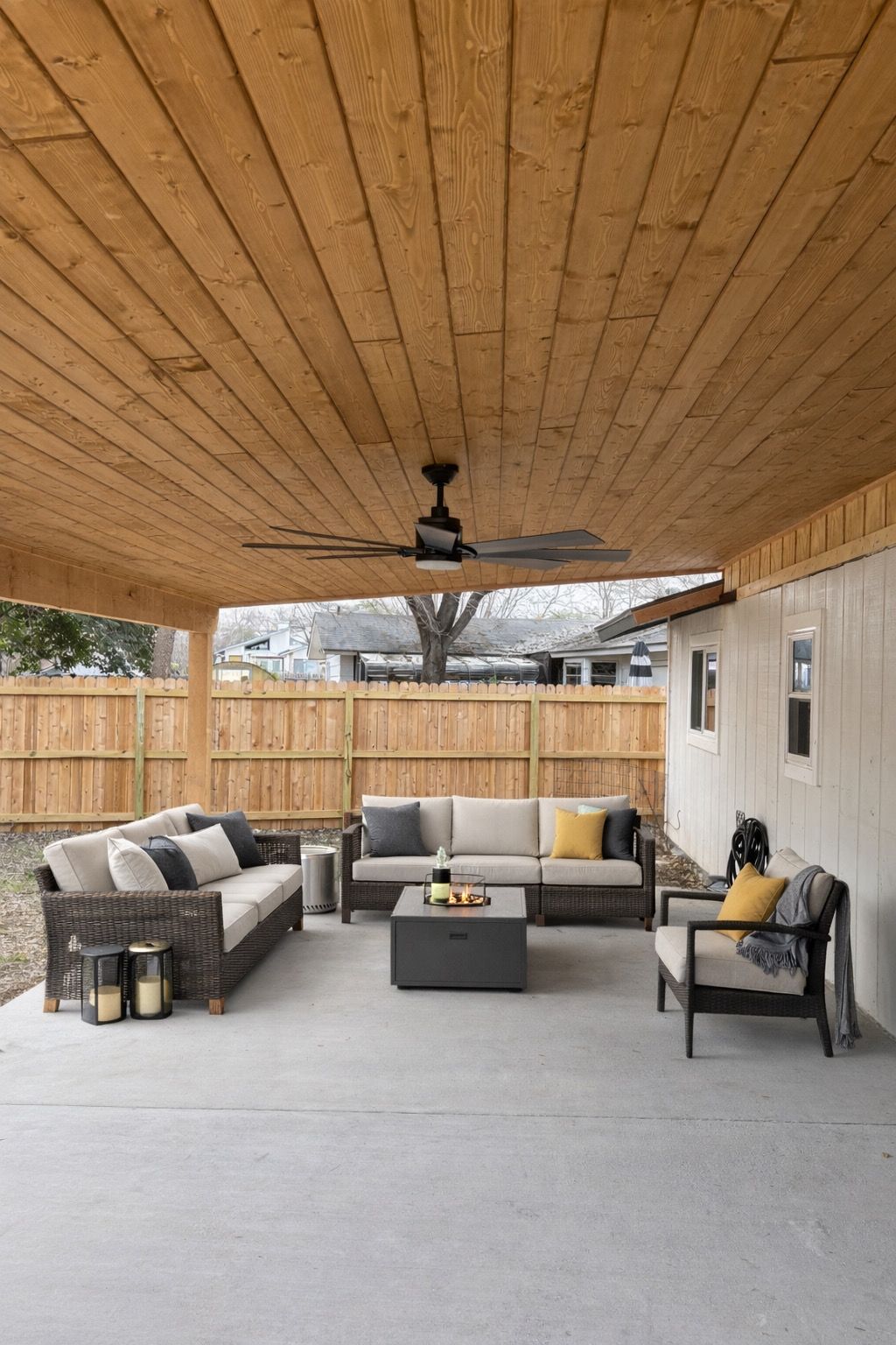 Covered patio with wicker seating, gray cushions, fire table, and ceiling fan on a concrete floor.