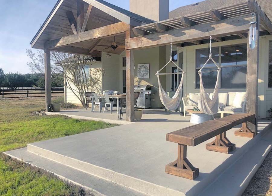 Modern porch with a bench, table, and chairs on a concrete patio beside a grassy field.
