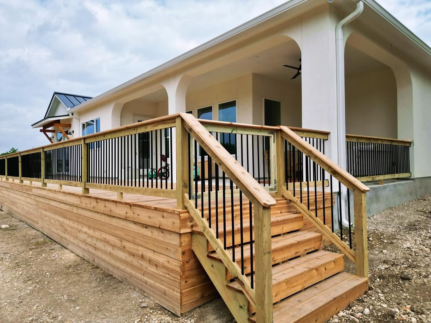 Porch with wooden stairs and black railing on a white house exterior