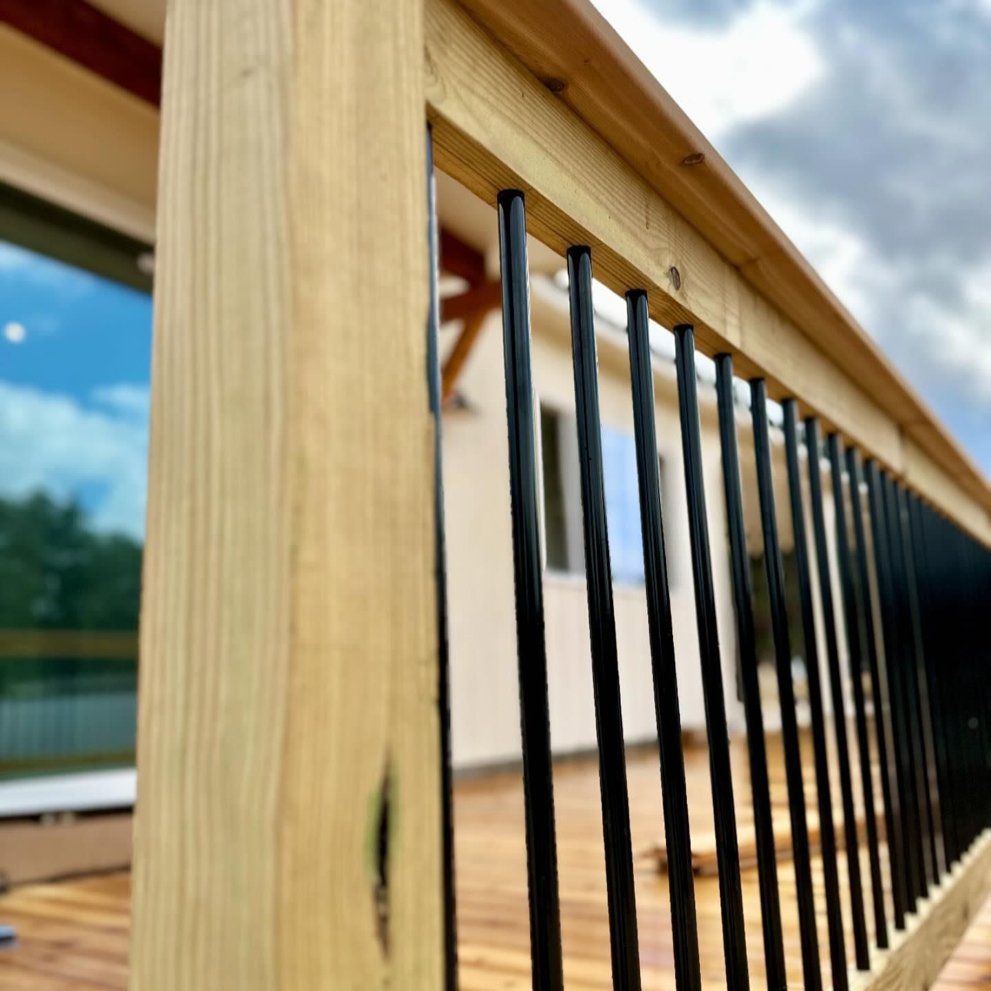 Close-up of a wooden deck railing with black metal balusters and a blurred outdoor view beyond