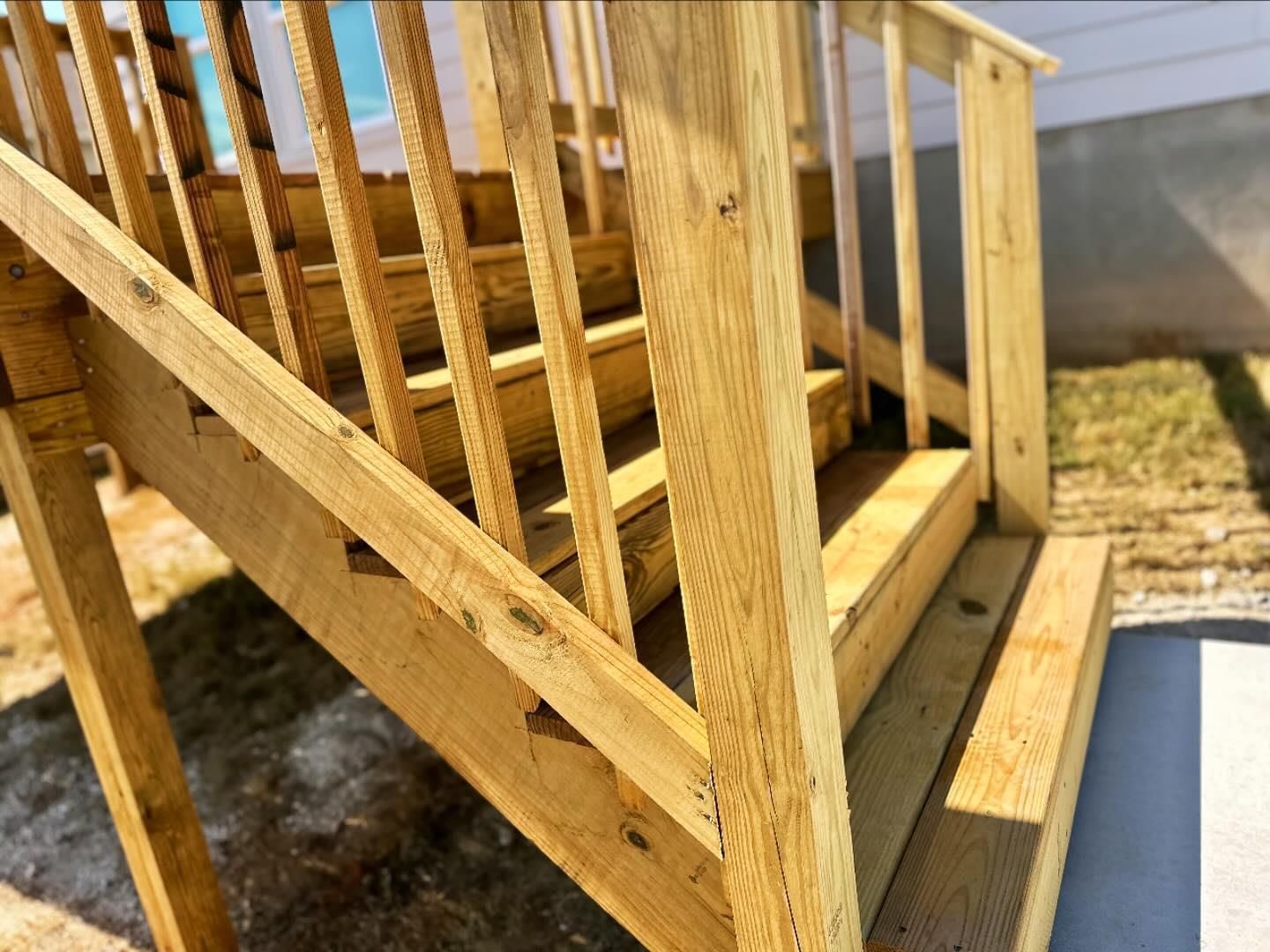 Wooden outdoor staircase with railings beside a house and a concrete walkway