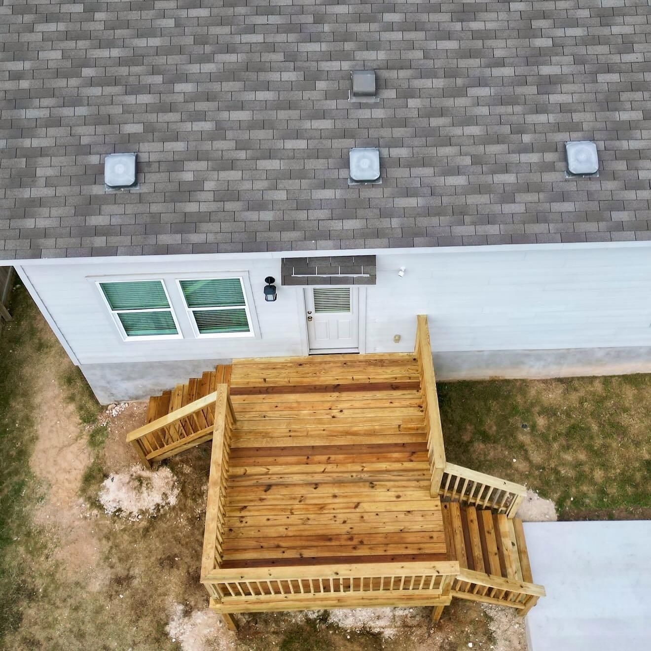 Aerial view of a house with a wooden deck and stairs leading to a white exterior door.