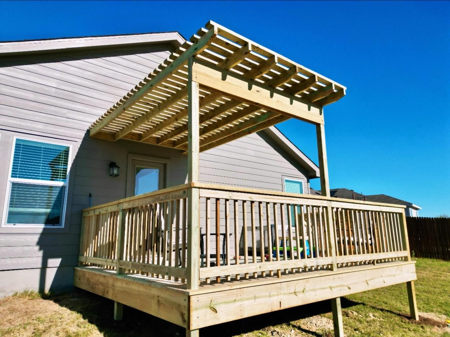 Wooden backyard deck with pergola attached to a house under a clear blue sky