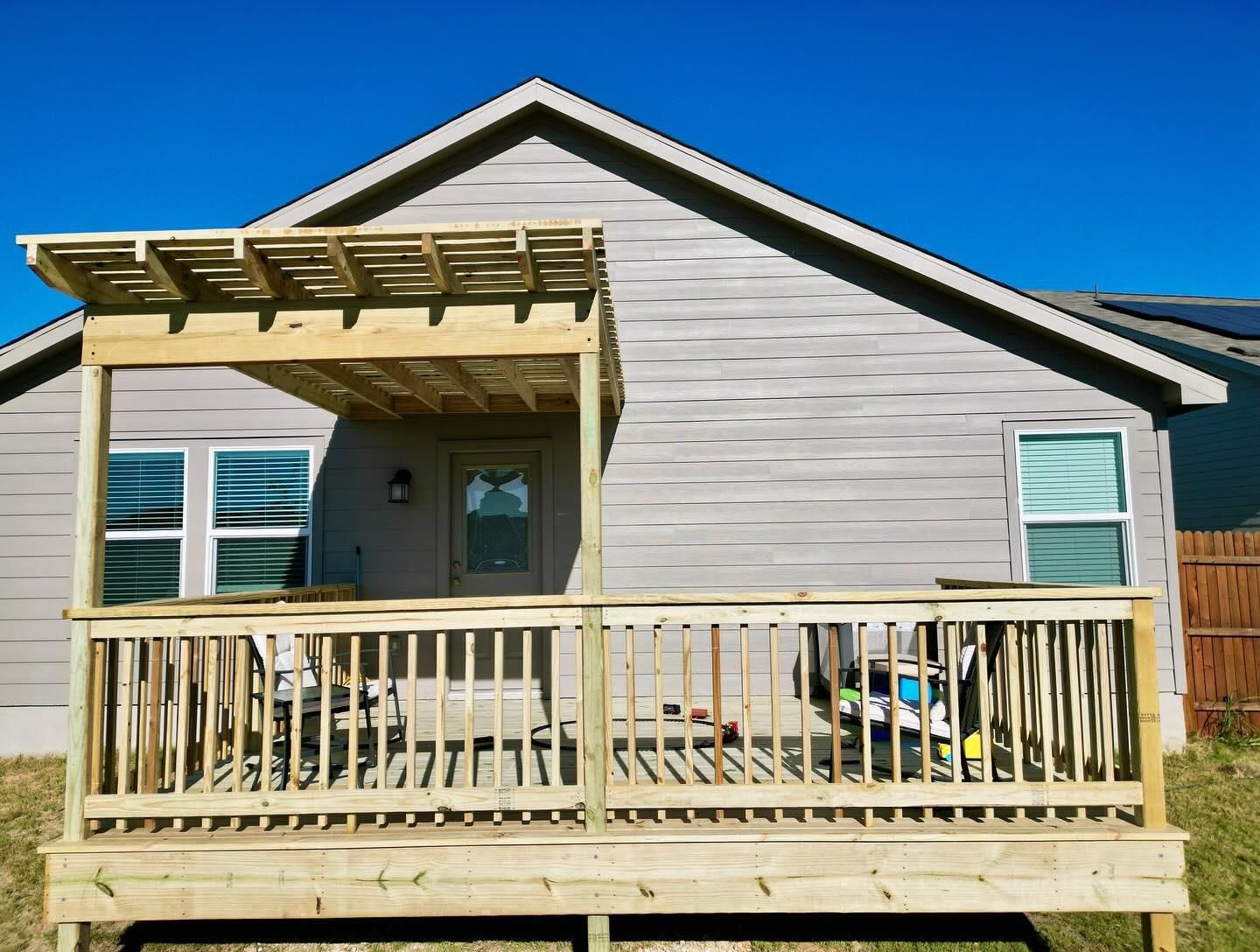 Small beige house with a wooden porch and pergola under a clear blue sky
