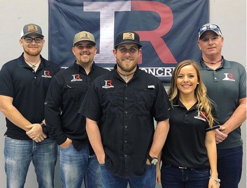 Five people in black polo shirts posing in front of a TR banner at an indoor event.
