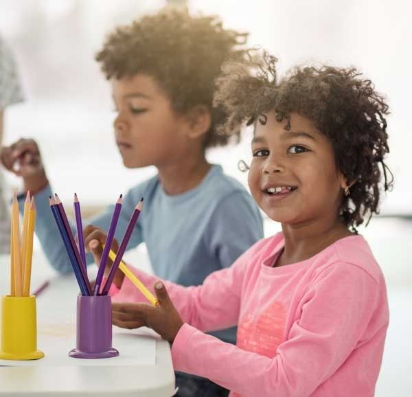 Two children coloring at a table with purple and yellow pencil cups