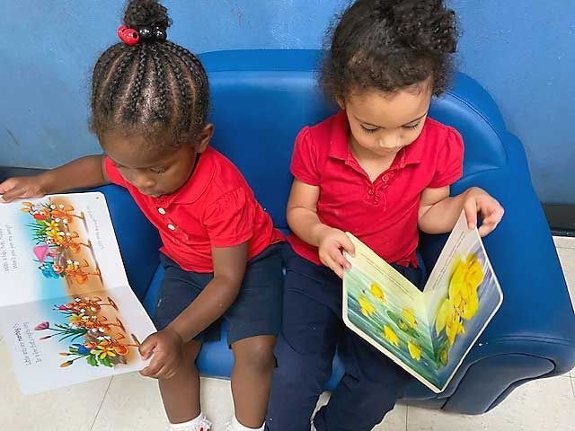 Two children in red shirts sit on a blue couch, reading colorful picture books.
