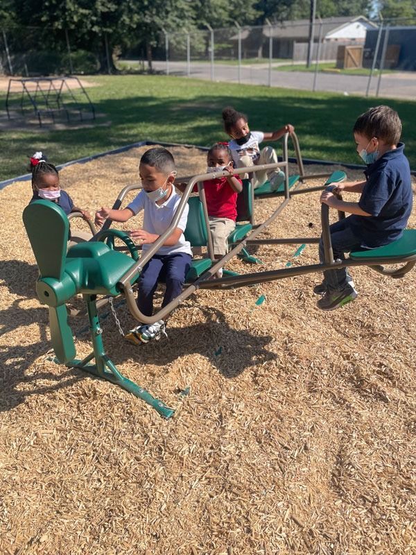 Children riding a green playground spinning seat on wood chips outdoors in a park