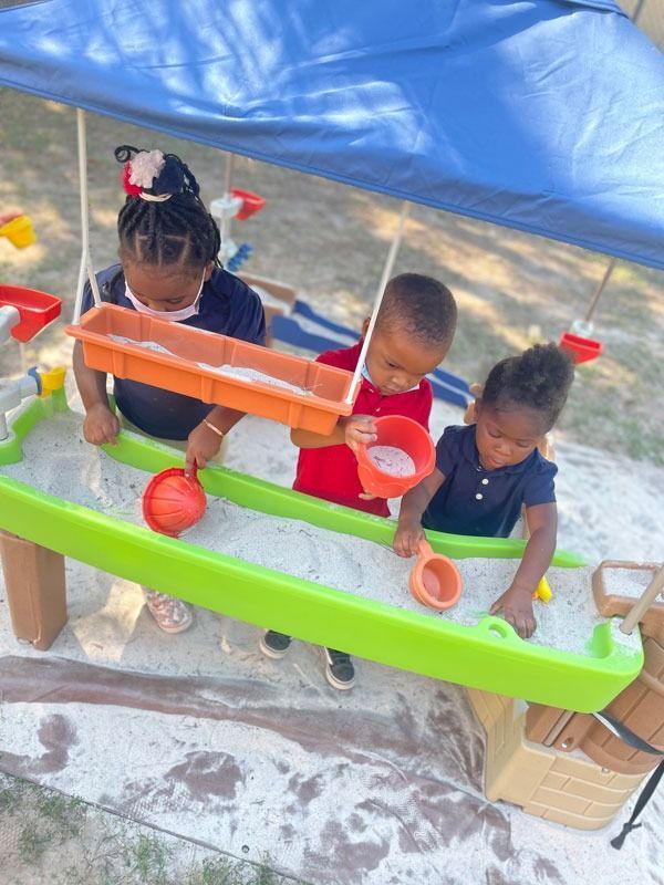 Children playing with colorful water toys under a blue tarp outdoors