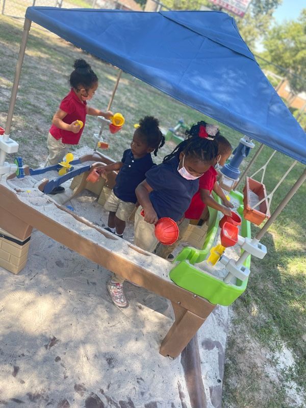 Children playing at a water table under a blue canopy with colorful cups and toys outdoors