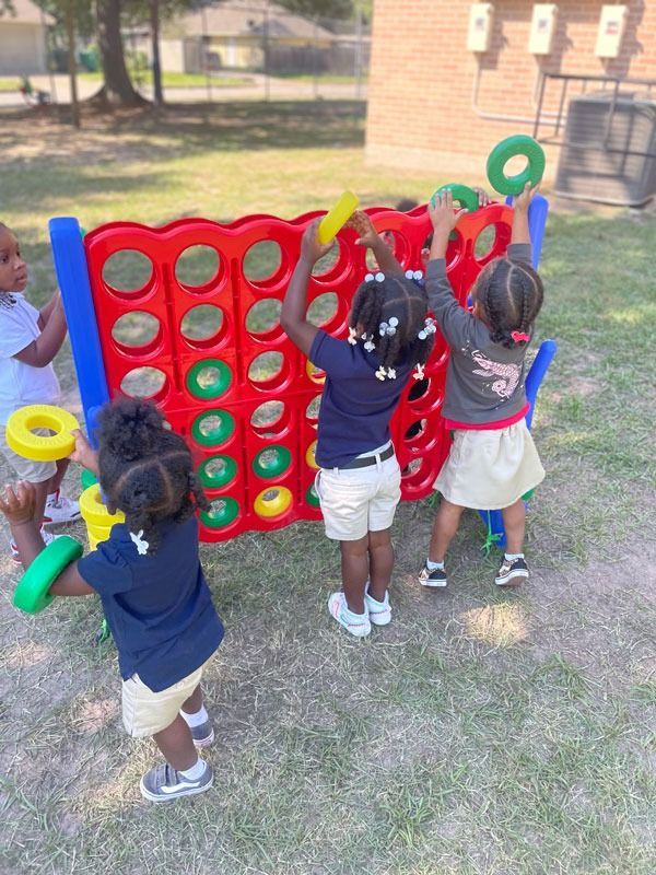 Children playing giant Connect Four outdoors on grass.