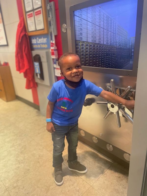 Smiling child in a blue shirt standing at a water fountain in a hallway