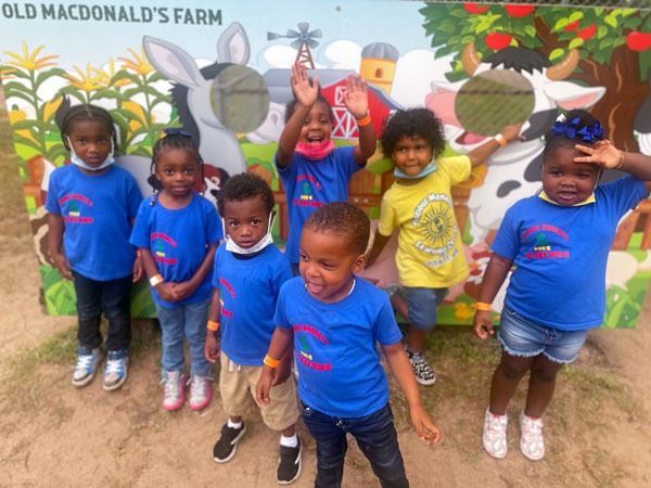 Children posing in front of a mural at Old MacDonald’s Farm, wearing blue and yellow shirts