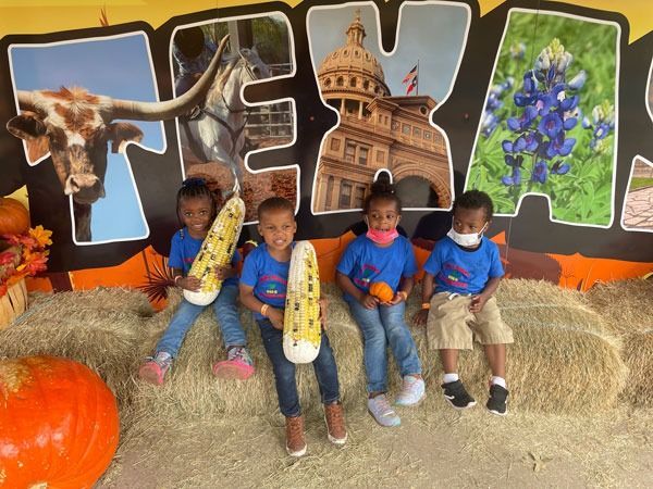 Four children sit on hay bales in front of a bright Texas-themed photo backdrop.