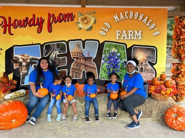 Group posing with pumpkins in front of a “Howdy from Texas” Old MacDonald’s Farm sign