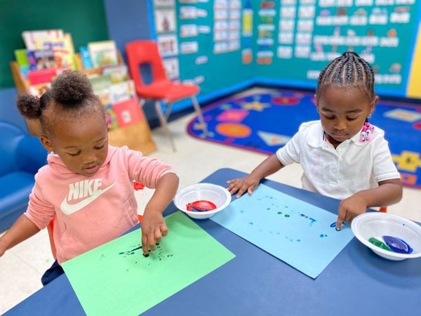 Two children painting at a table in a colorful classroom