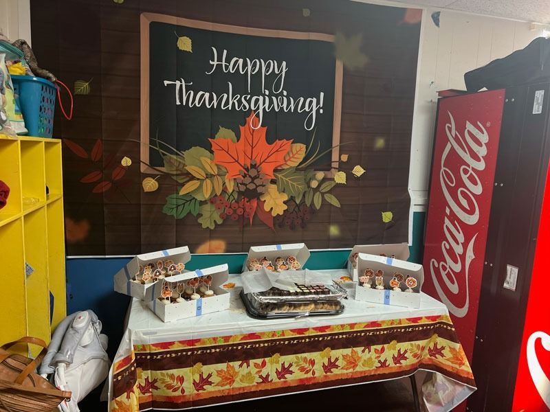 Thanksgiving dessert table with pumpkin decor and “Happy Thanksgiving!” sign beside a Coca-Cola cooler