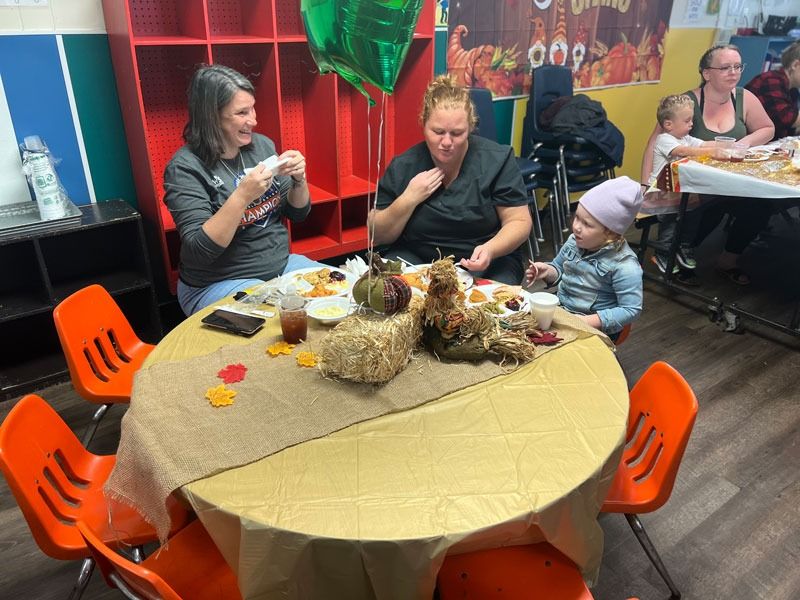 People seated around a round table with craft materials in a colorful classroom or activity room