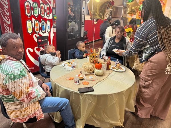People gathered around a decorated table at a party, with food, drinks, and balloons in a festive room.