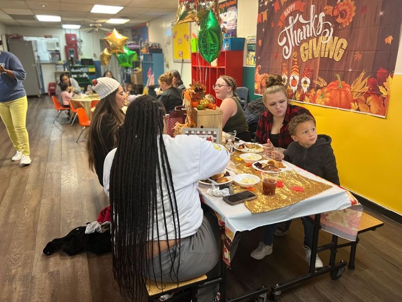 People seated at a long table at a festive Thanksgiving meal in a decorated cafeteria.