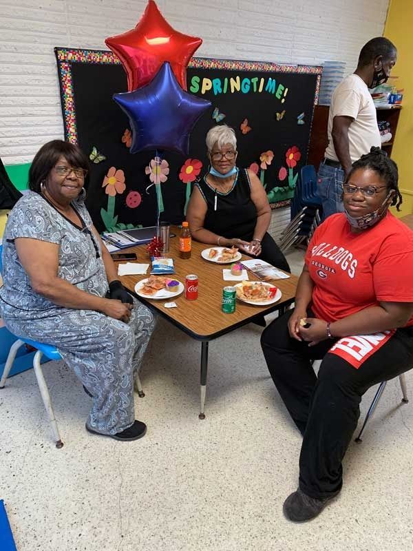Three people seated at a decorated springtime table with balloons and flowers in a community room.