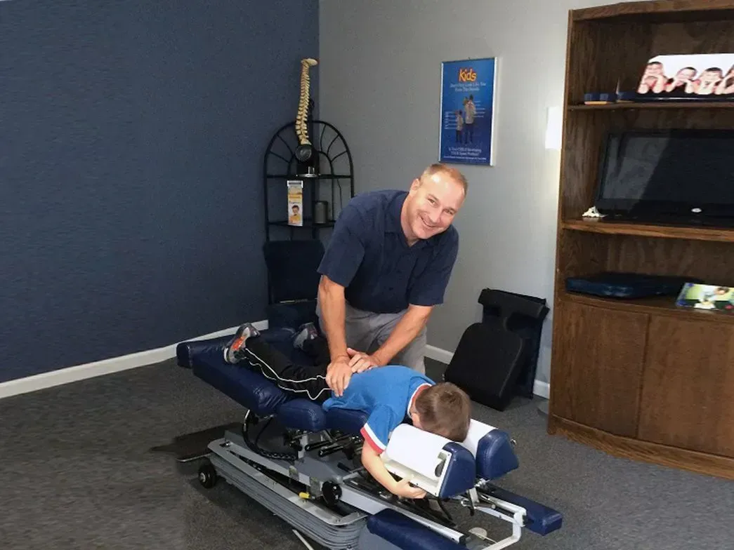 Chiropractor adjusting a child on an adjusting table in an office setting.