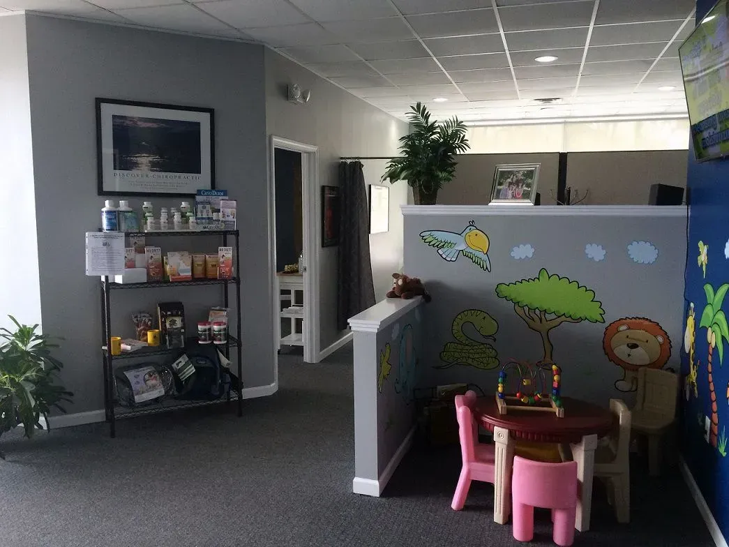 Reception area with gray walls, shelving with snacks, a small table and chairs, and a desk with child-friendly artwork.
