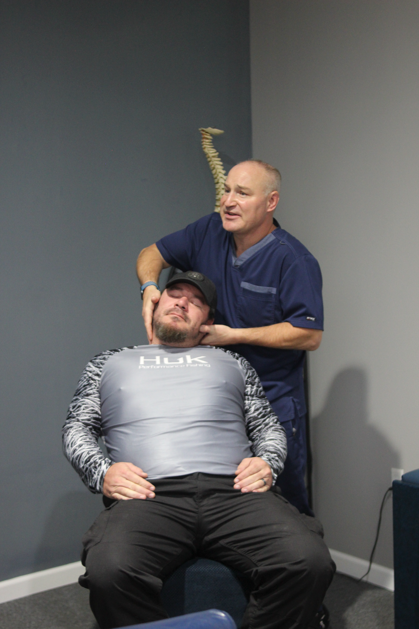Chiropractor adjusting a patient's neck in an office setting. Both men are looking forward.