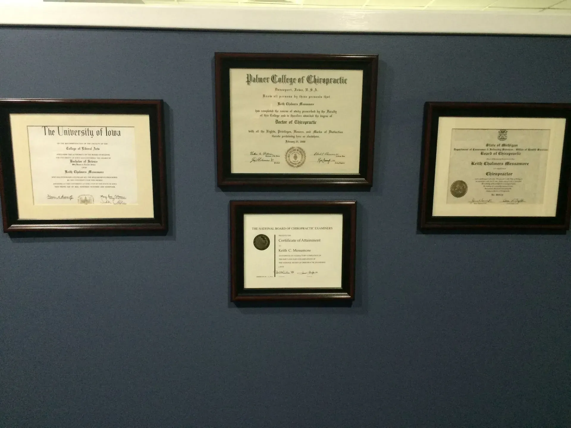Four framed diplomas on a blue wall.
