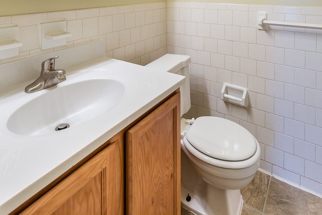 Small white bathroom with a sink, wooden vanity, and toilet against tiled walls.