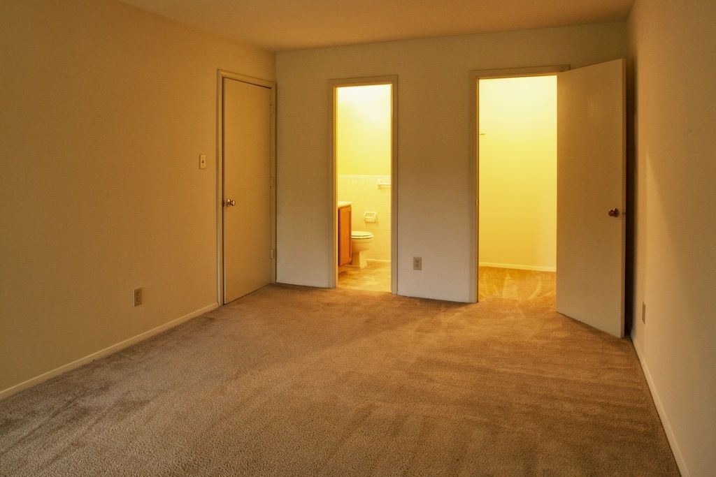 Empty beige carpeted room with two open doorways glowing warm yellow light