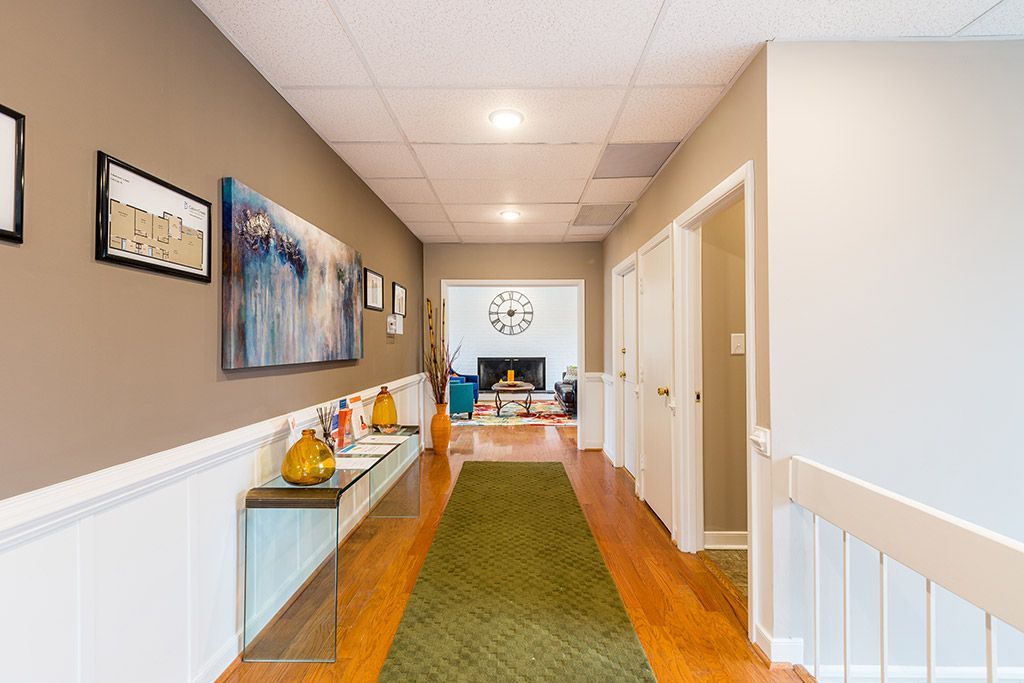 Bright hallway with tan walls, white trim, hardwood floor, and framed art leading to a living room.