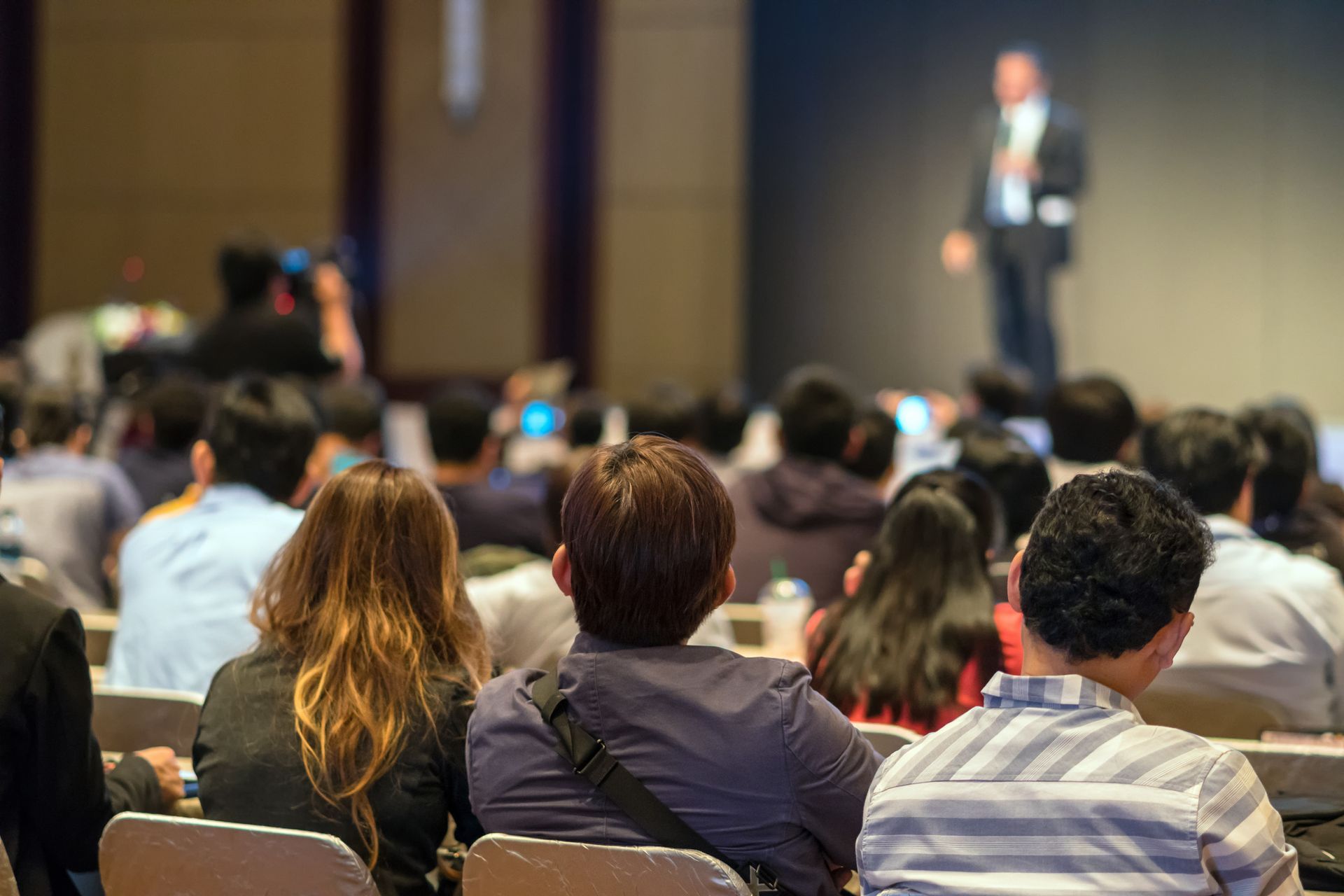 Audience seated at a conference, listening to a speaker on stage