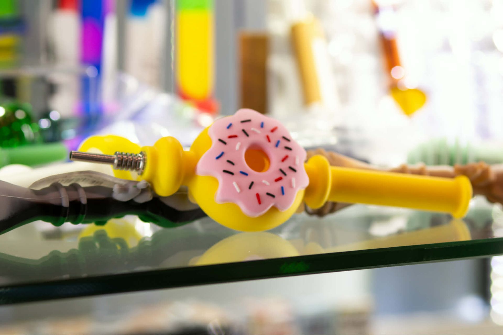 Yellow-and-pink donut-shaped object on a glass shelf with blurred colorful items in the background