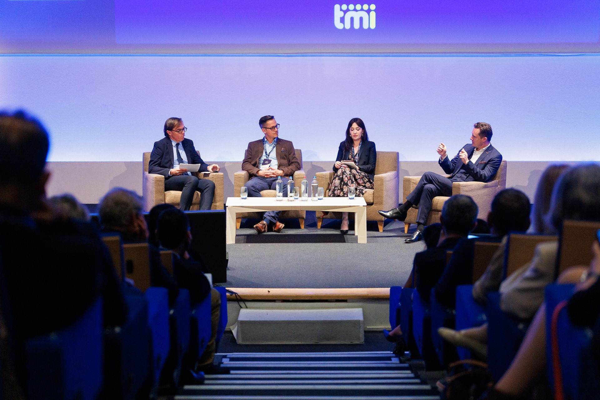 Table ronde sur scène lors d'une conférence, avec quatre intervenants assis sous un écran éclairé en violet.