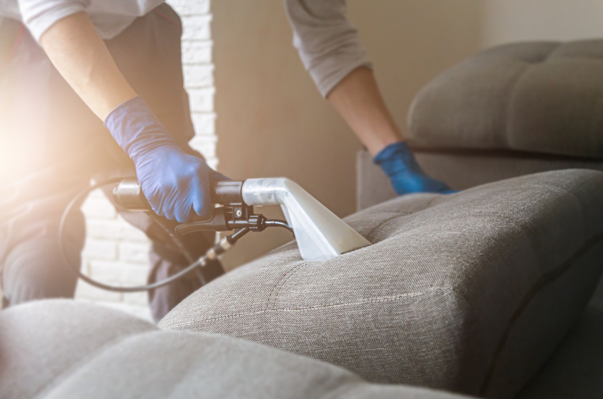 Worker using a steam cleaner on a gray sofa in a living room